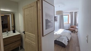 Une chambre avec une porte en bois, un lit avec une literie blanche, une chaise et une fenêtre avec des rideaux.