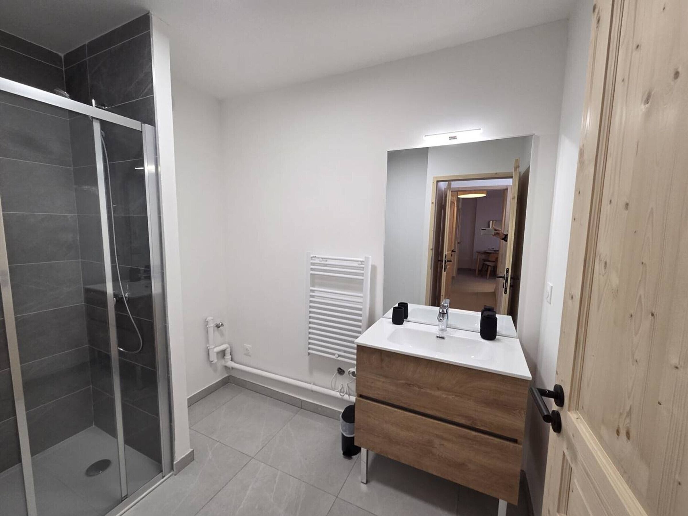 Een moderne badkamer met een douchecabine van glas, een witte wastafel met spiegel en een houten wastafelmeubel.