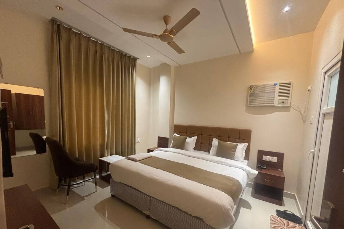 A hotel room with a large bed, a desk, a chair, a ceiling fan, and an air conditioning unit.