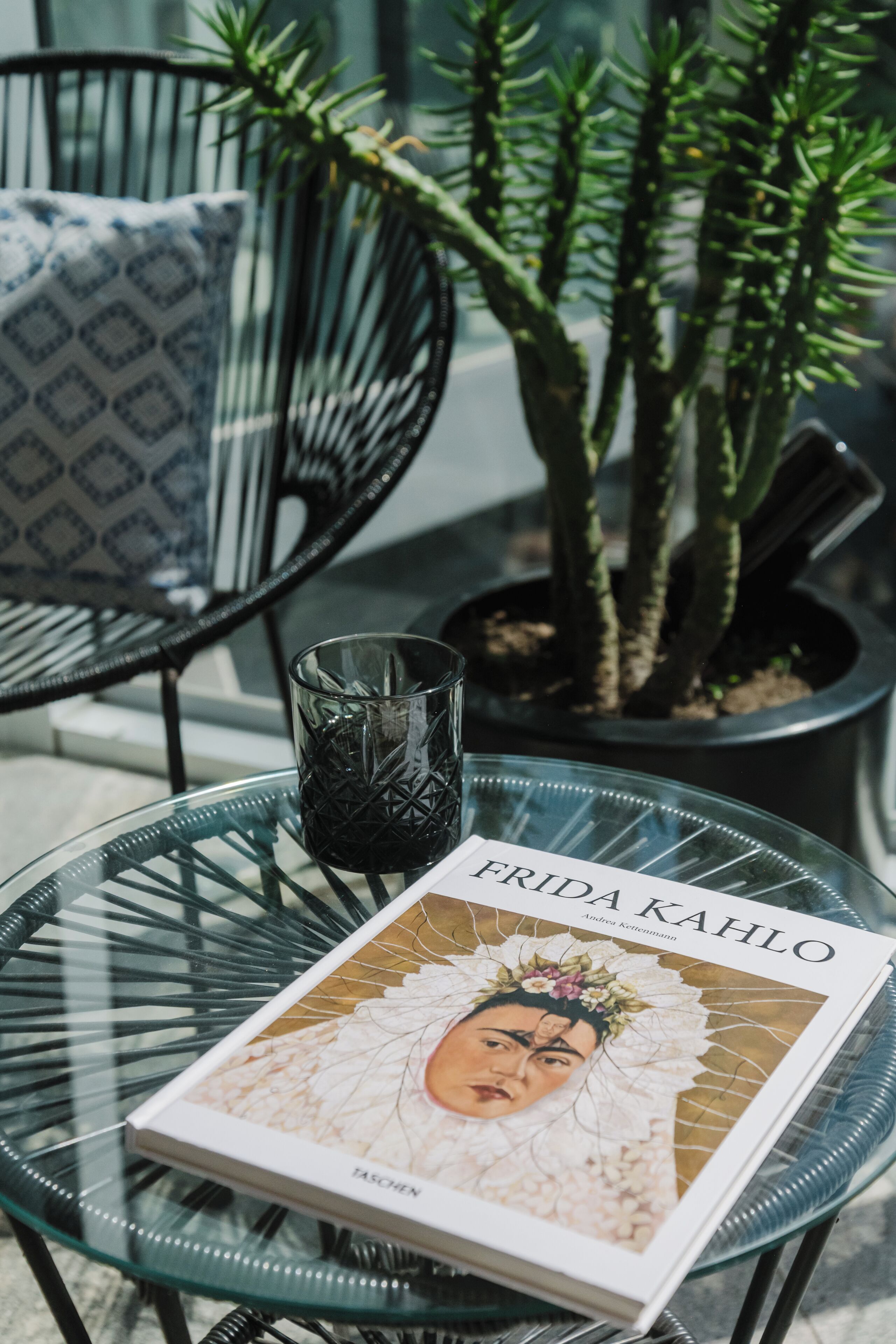 Una mesa de vidrio con un libro titulado "FRIDA KAHLO" y un candelabro de vidrio.