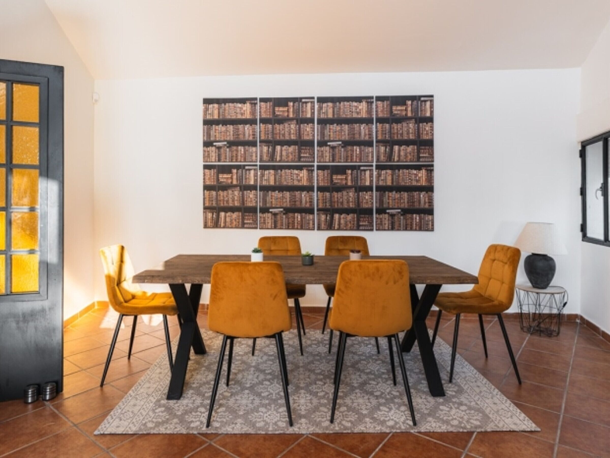 A dining area with a wooden table and six chairs, a bookshelf, and a lamp.