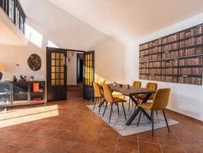 Un vaste espace dédié à la salle à manger, avec une longue table en bois et des chaises jaunes, une bibliothèque remplie de livres et un escalier menant à un niveau supérieur.