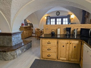 A rustic kitchen with wooden cabinets, a stone countertop, and a window with curtains.