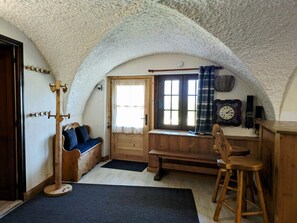 Ein gemütliches Zimmer mit einer Holzbank, einem Holzschemel, einer Uhr und einem Fenster mit Vorhängen.