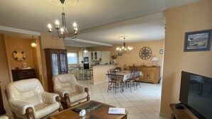 A spacious living area with leather sofas, a coffee table, and a TV. A kitchen with a dining area is visible in the background. - Ground floor T3 apartment, near Crouesty port, wifi, parking (Arzon)