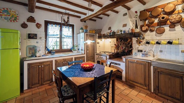 Une cuisine rustique avec des poutres en bois, une table à manger avec des chaises, un réfrigérateur vert, ainsi que divers ustensiles de cuisine et objets décoratifs accrochés aux murs.