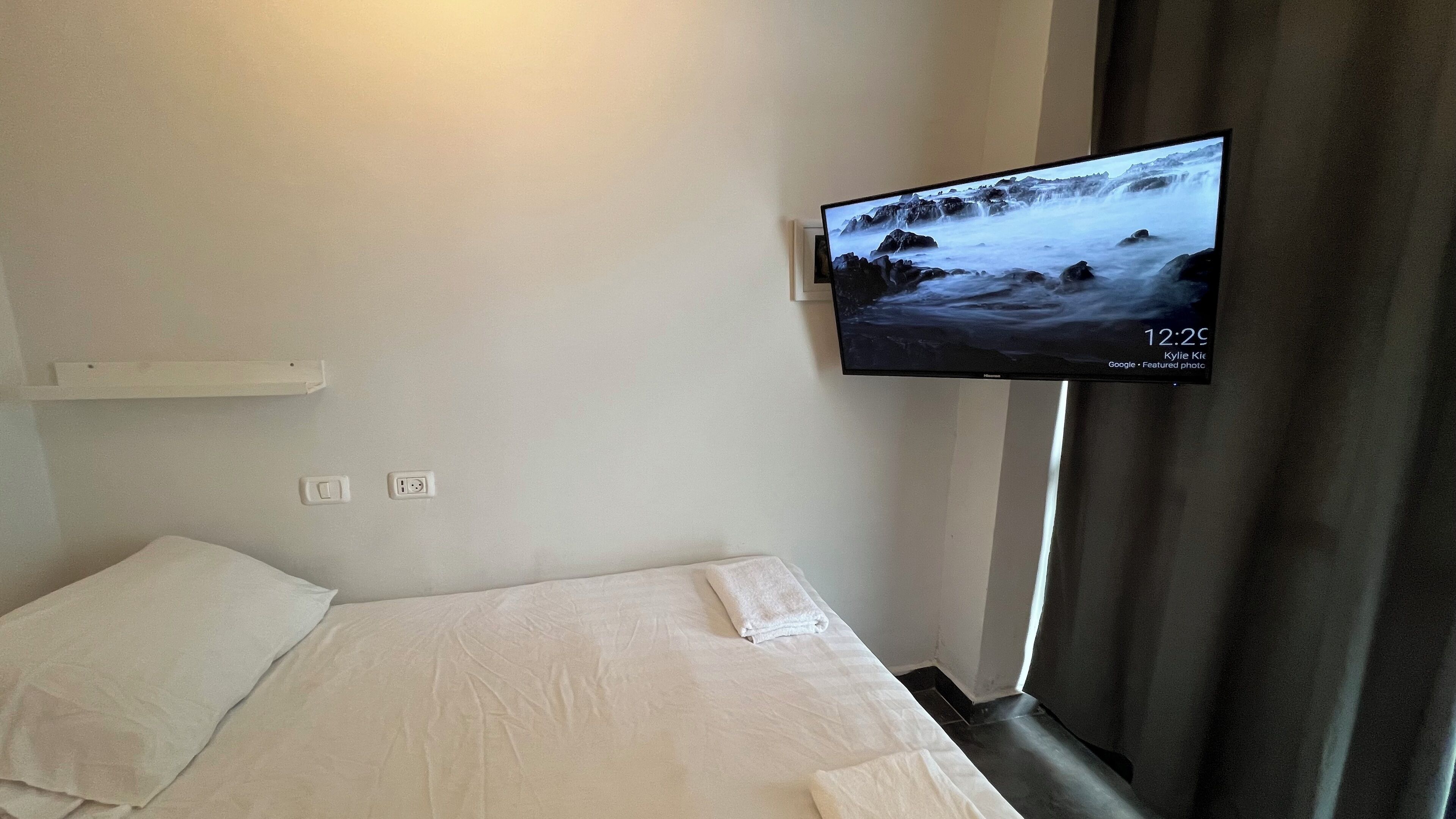Une chambre d’hôtel avec un lit, un téléviseur fixé au mur diffusant des images de la nature, et une fenêtre avec des rideaux.