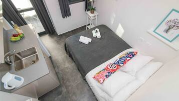 A hotel room with a bed, a small desk with a sink, a window with curtains, and a wall with a framed picture.