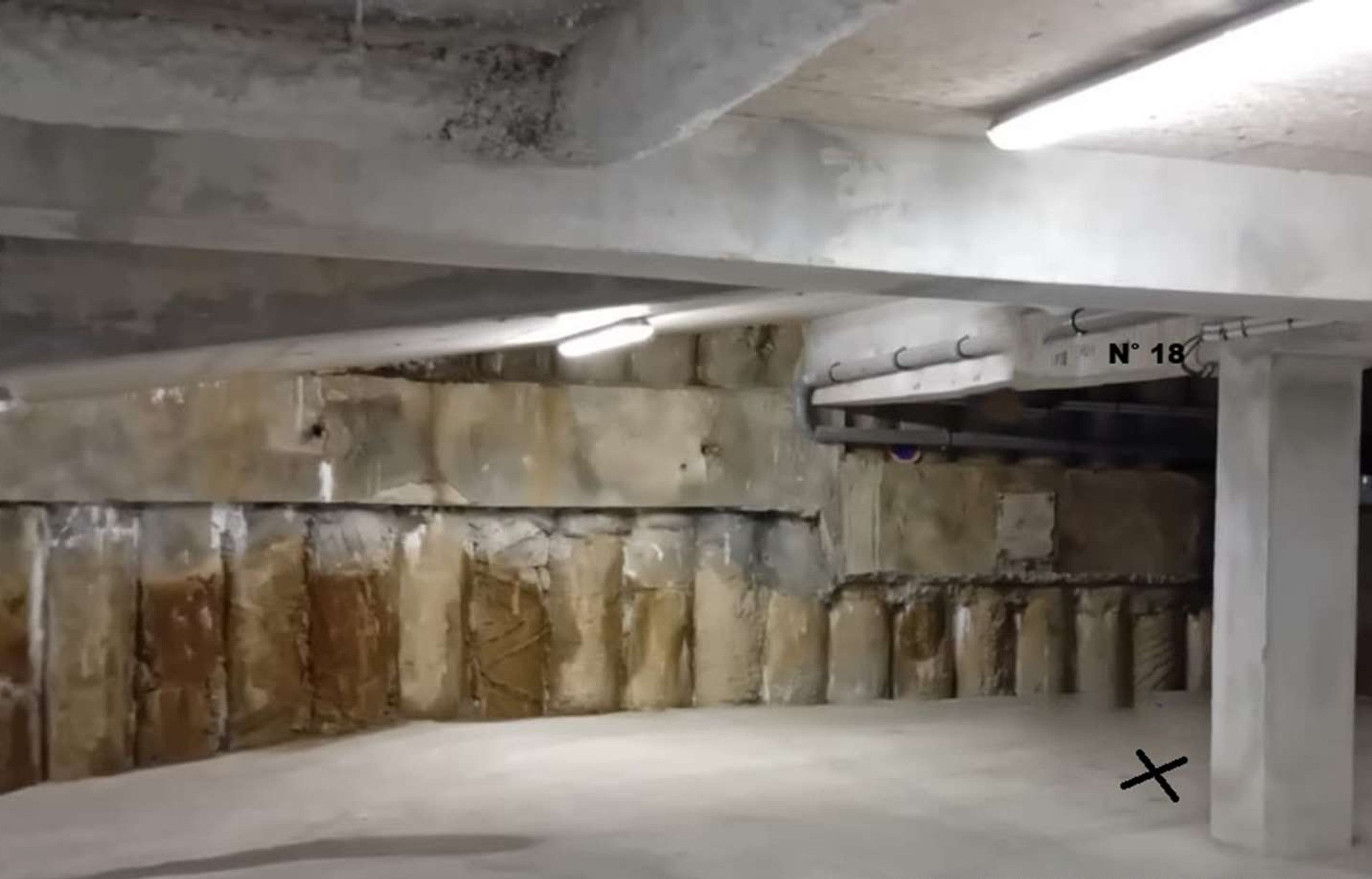 A parking garage with concrete walls, a ceiling with fluorescent lighting, and a sign indicating "N° 18".