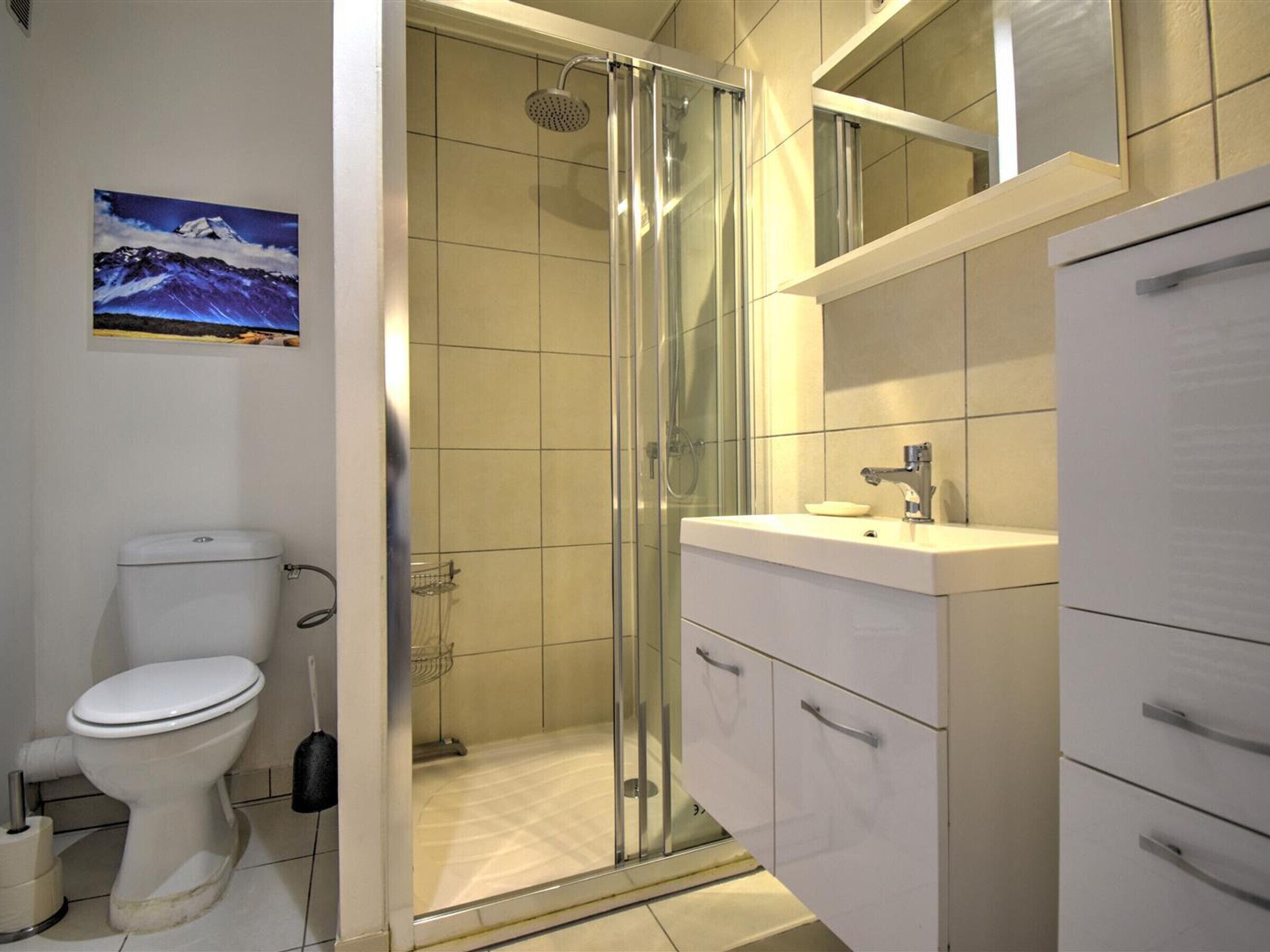 Un baño moderno con ducha envuelta en vidrio, inodoro y tocador con cajones.