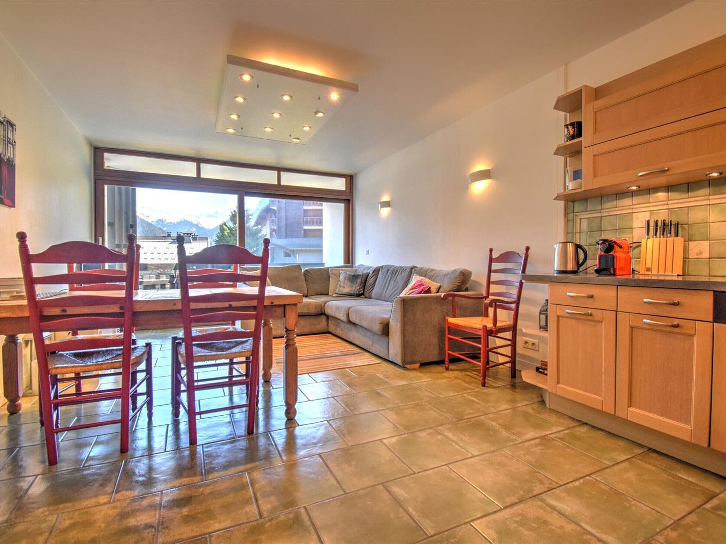 A modern kitchen with a dining area, a sofa, and a view of the outdoors.