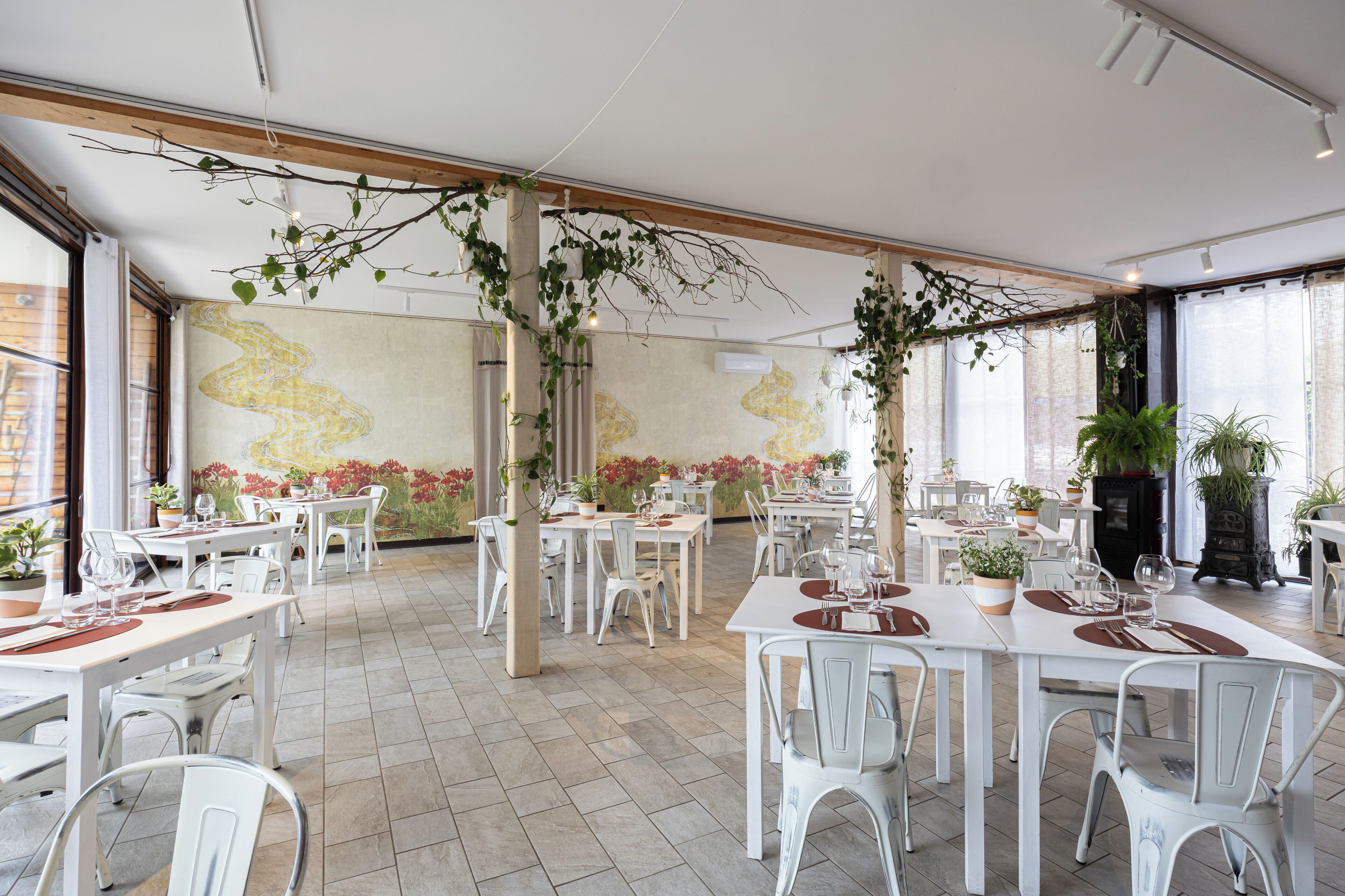 Un restaurant amb taules i caires blanques, plantes en testos i un mural a la paret.