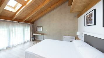 Une chambre à coucher avec un grand lit, des poutres apparentes en bois au plafond, un bureau et une fenêtre avec des rideaux.