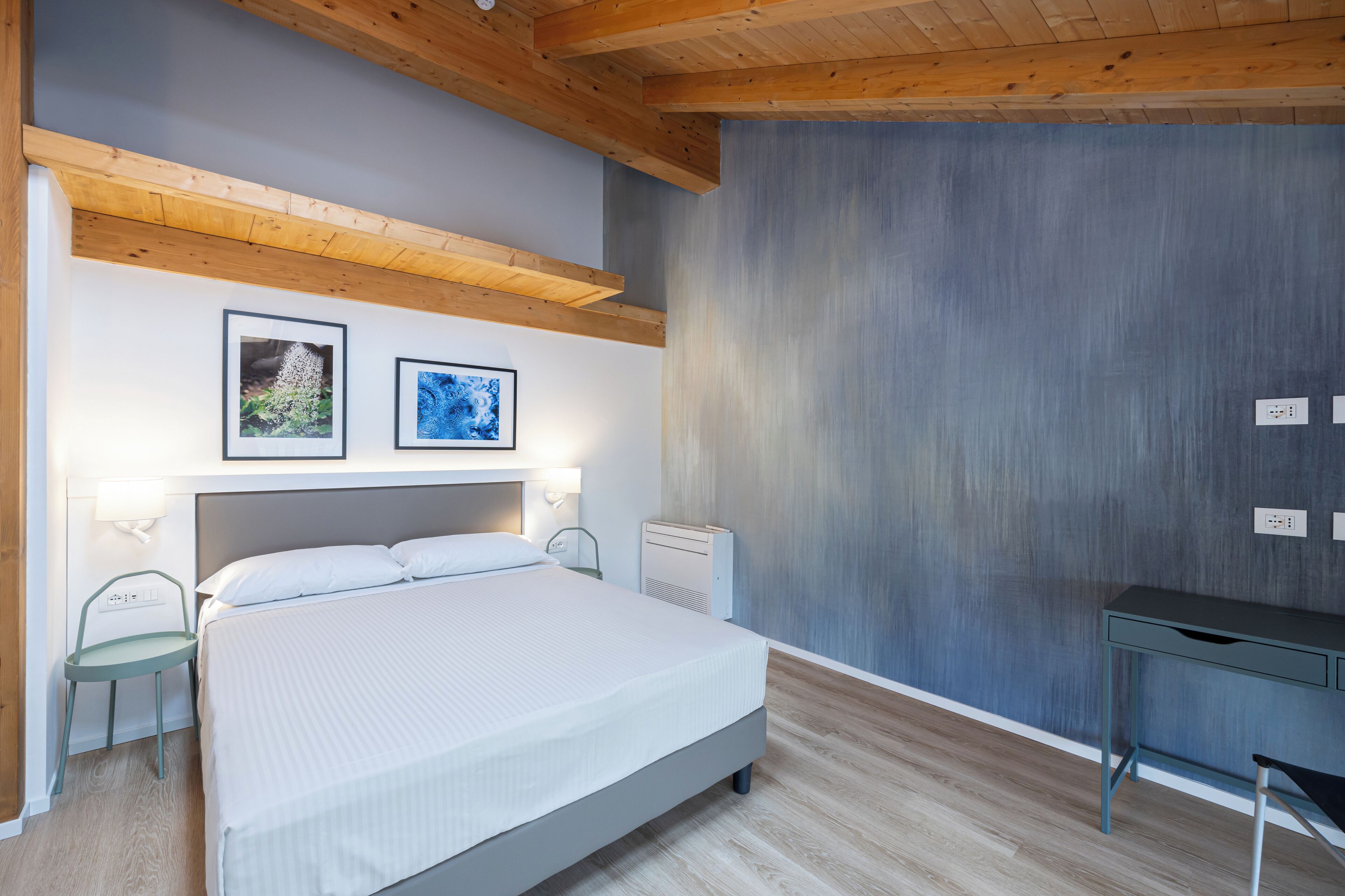 Un dormitorio con cama, mesitas de noche, un escritorio y dos cuadros en la pared.