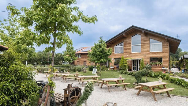 A rustic wooden house with a garden patio area featuring picnic tables and a vintage tractor. - Agriturismo Sadira  (Calusco d'Adda)