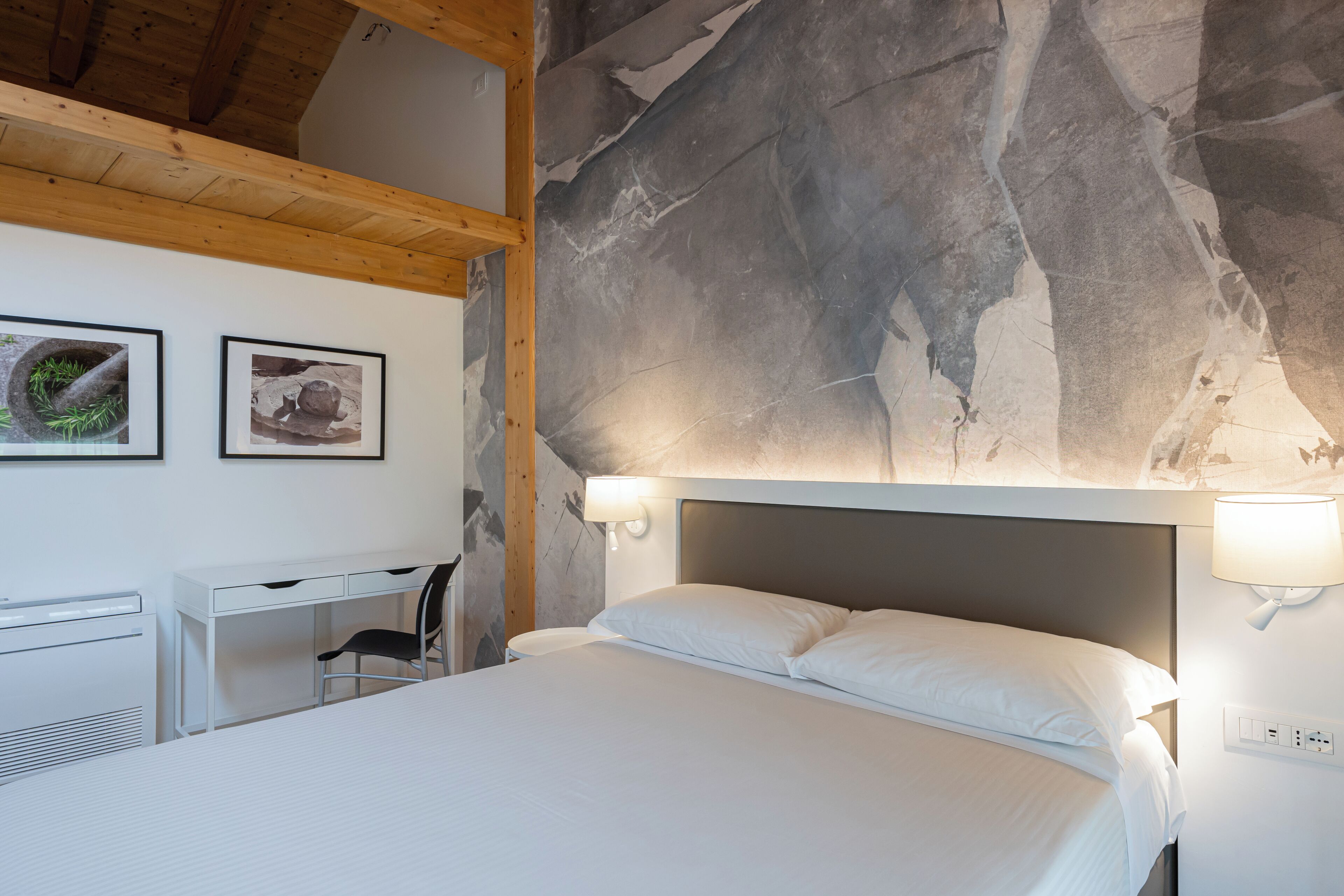 Quarto com cama, escrivaninha e duas luminárias na parede.
