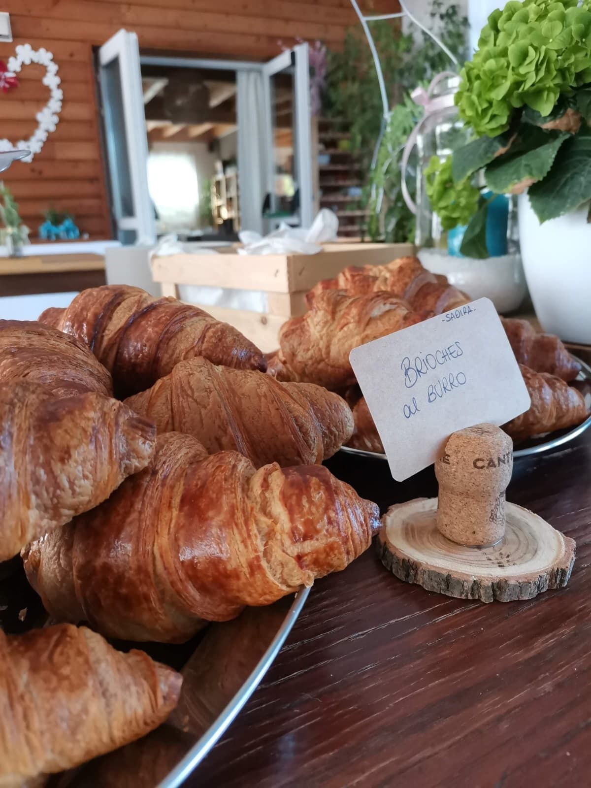 Una bandeja de croissants sobre una mesa de madera con un cartel que dice 'Brioches al burro'.