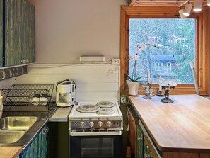 A kitchen with a stove, sink, and a window with a view of trees and houses. - 4 Person Holiday Home in Tyreso (Tyreso)