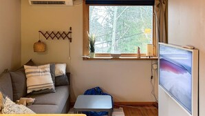 A cozy living room with a sofa, a small table, a TV, and a window with a view of trees. - 4 Person Holiday Home in Tyreso (Tyreso)