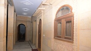 A corridor with ornate wall decorations, a marble floor, and a wooden door at the end. - Khushbu haveli hotel and restaurant (Pokhran)