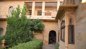 A courtyard with a traditional building, a small tree, and a statue. - Khushbu haveli hotel and restaurant (Pokhran)