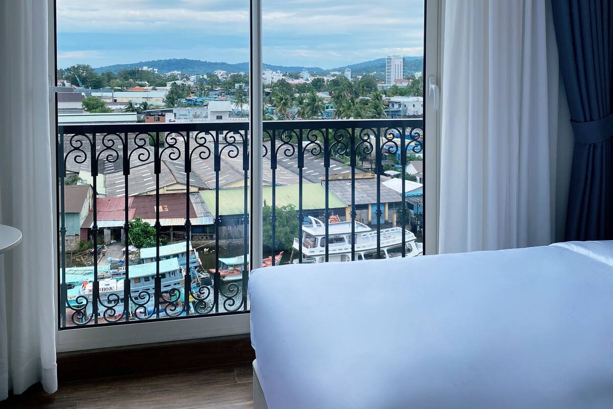 A hotel room with a large window, a bed, and a view of a cityscape.