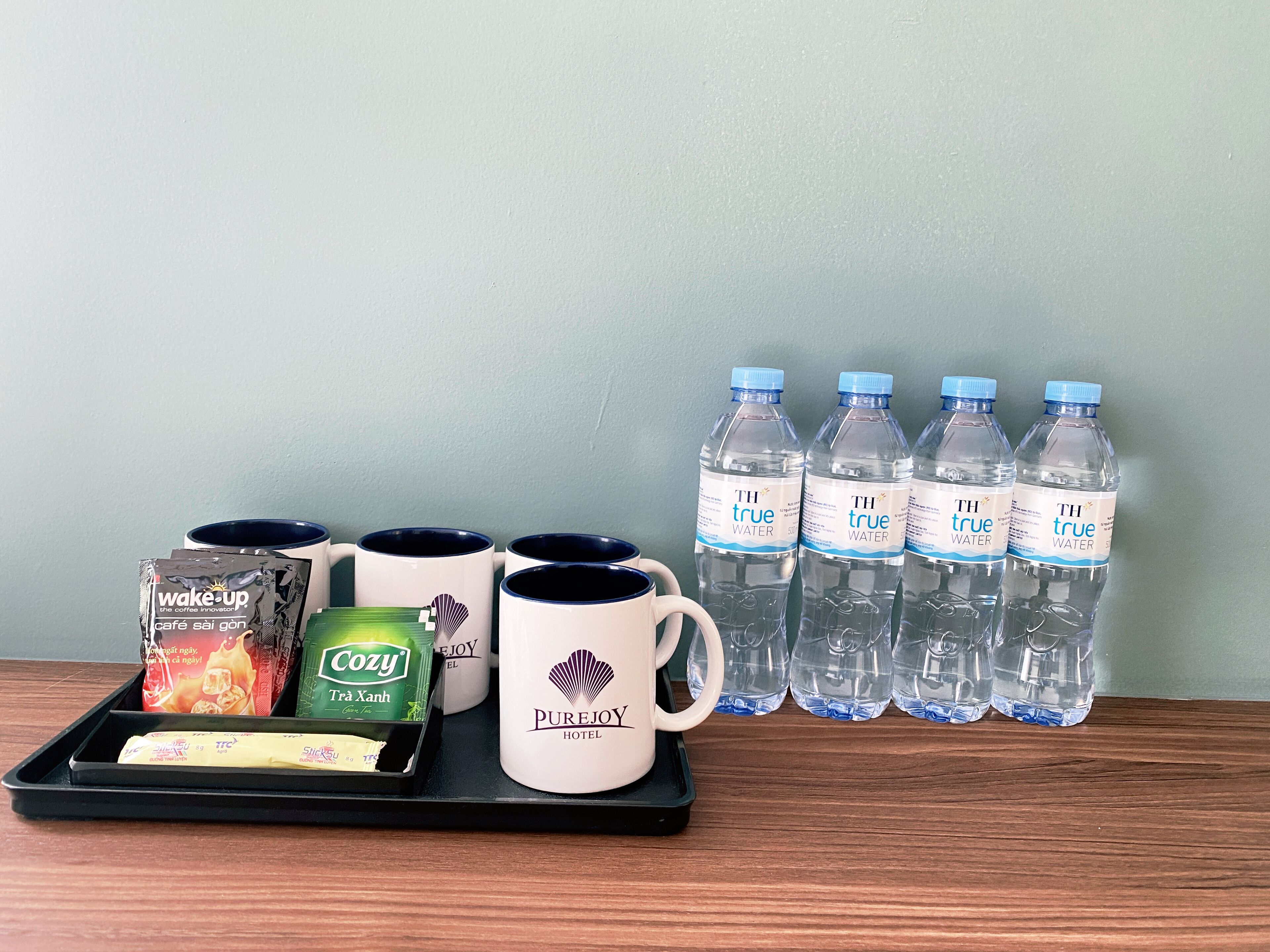 Una bandeja con sobres de café, una taza y una botella de agua, todo sobre un fondo con botellas de agua.