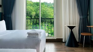 A hotel room with two beds, a small table, and a chair. The room has a balcony with a view of greenery. - PureJoy Hotel City Center Phu Quoc (Phu Quoc)