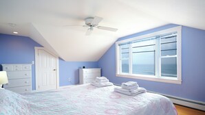 A bedroom with a bed, a ceiling fan, a dresser, a window with a view, and a door. - Ocean views galore. York Beach at your finger tips (York Beach)