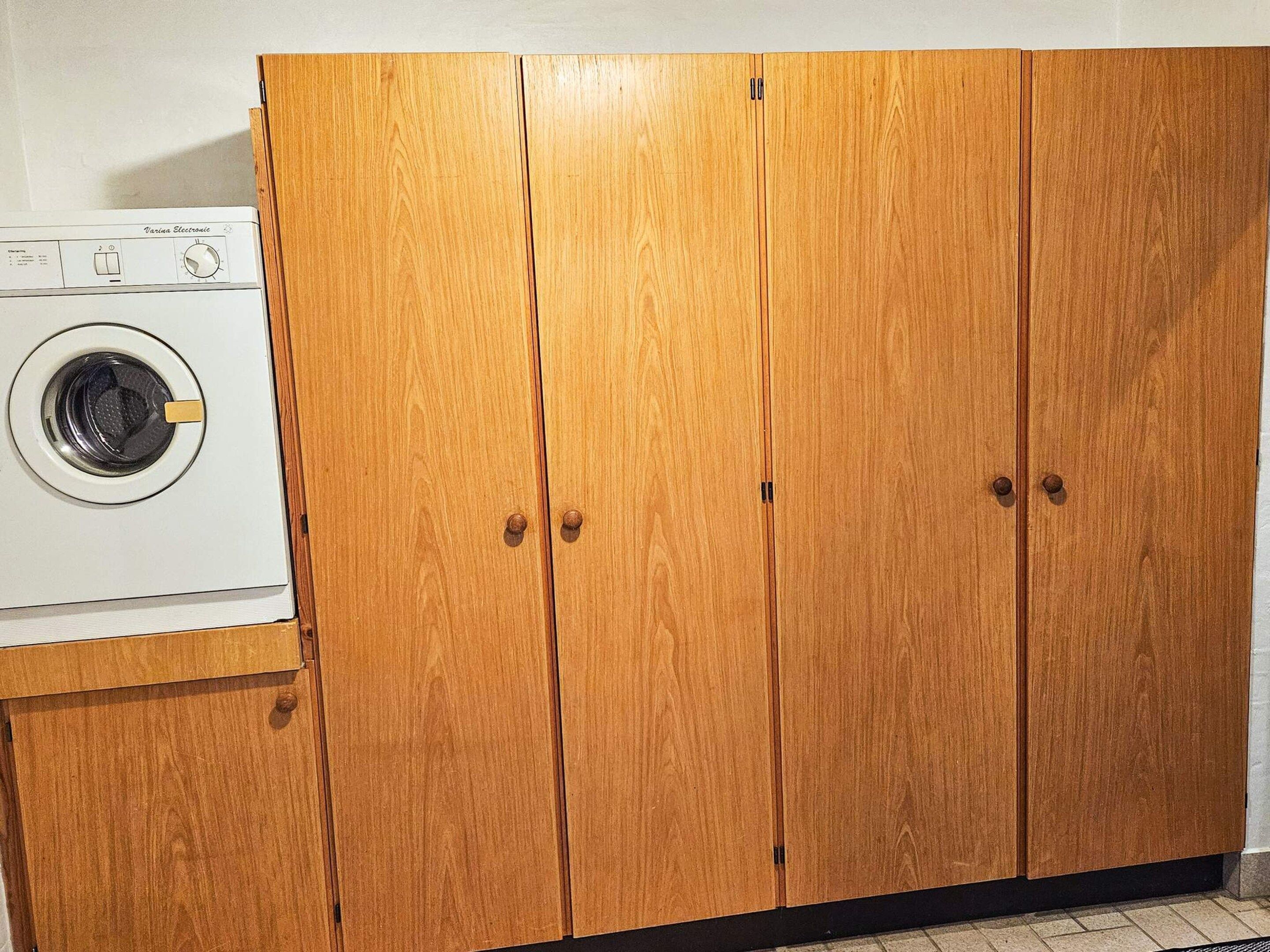 A compact laundry area with a front-loading washing machine and a wooden wardrobe with two doors.