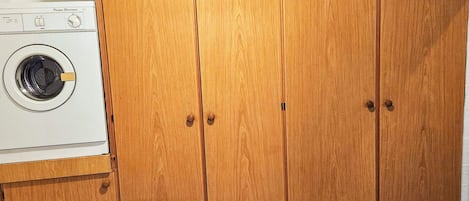Un área de lavandería compacta con lavadora de carga frontal y un armario de madera con dos puertas.