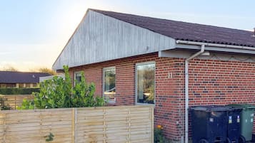 A residential building with a sloped roof, brick walls, and a wooden fence.
