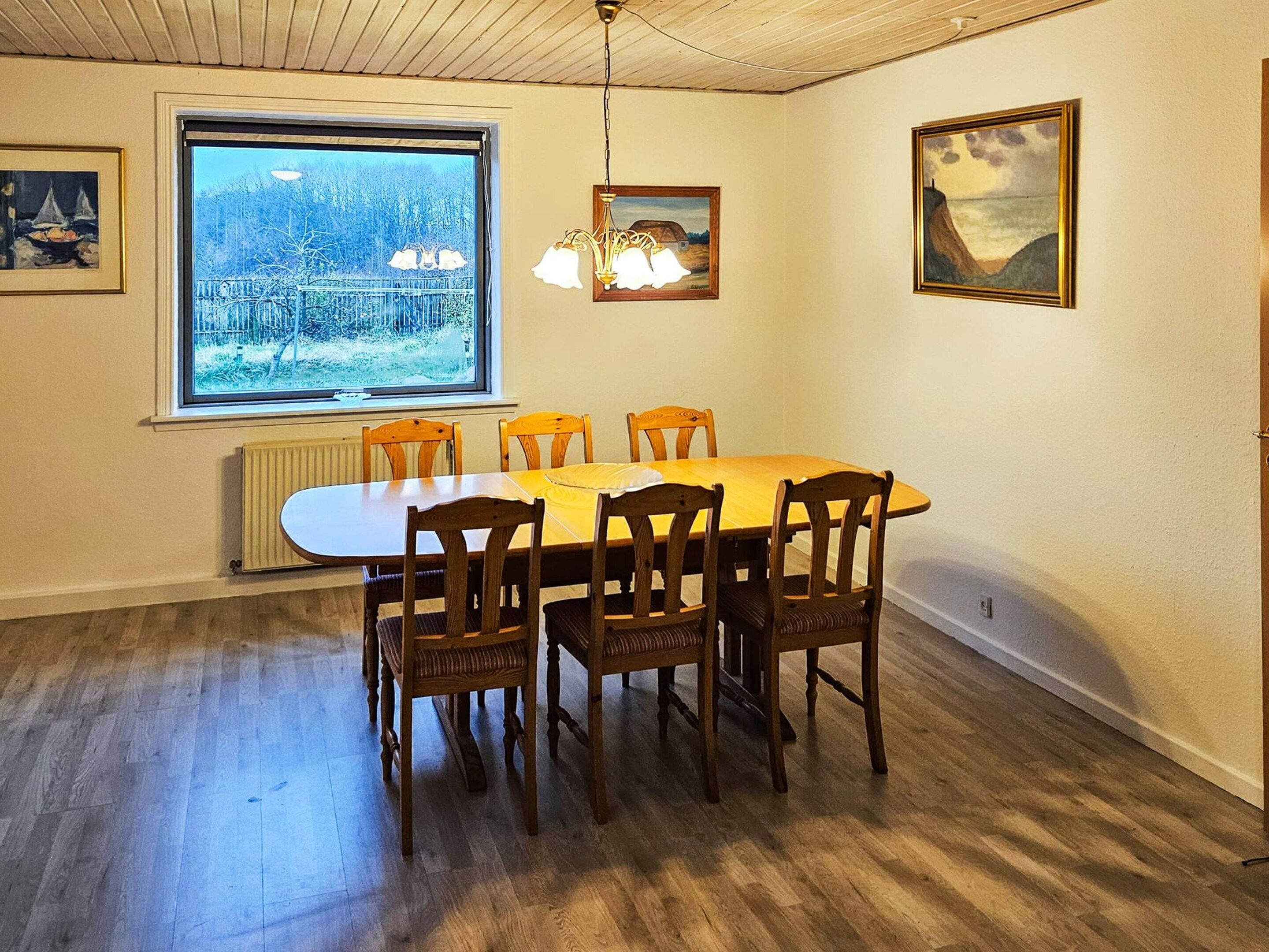 Ein Esszimmer mit großem Fenster, Holzsesseln, einem Tisch und einer Hängelampe.