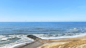 A coastal landscape with a sandy beach, waves, and wind turbines in the distance.