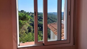 Une fenêtre donnant sur un paysage verdoyant et luxuriant, avec des toits couverts de tuiles en terre cuite.