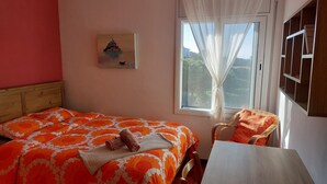 Une chambre à coucher avec un lit, une chaise, une table, un tableau et une fenêtre avec des rideaux.