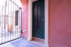 Una puerta verde cerrada con una reja metálica al frente, una pared rosa y una base de piedra.