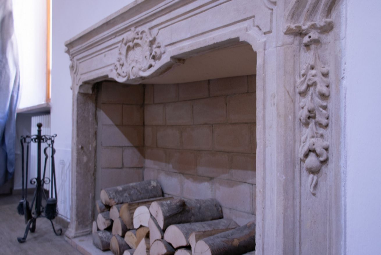 Una chimenea con leña apilada, un atizador de hierro forjado y una pared de piedra.