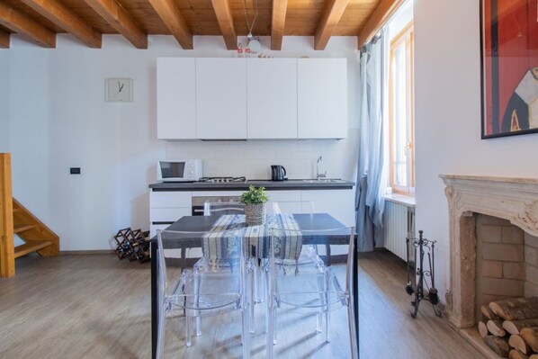 Una cocina moderna con armarios blancos, una mesa de comedor con sillas transparentes, una chimenea y una escalera de madera.