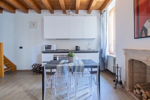 A modern kitchen with white cabinets, a dining table with clear chairs, a fireplace, and a wooden staircase.