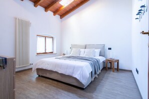 A bedroom with a bed, a window, a radiator, and a wooden ceiling. - GuestHost - A splendid 65 sq m apartment, perfect for 4 guests, located on the first floor of a completely renovated period building.The accommodation is located in Valeggio sul Mincio, just an 8-minute walk from the Scaligero Castle, a 15-minute walk fr (Valeggio sul Mincio)