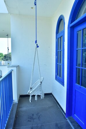 A balcony with a white hanging chair, blue-framed windows, and a white door. - Aaradhyam Resort and Spa (Garhmukteshwar)