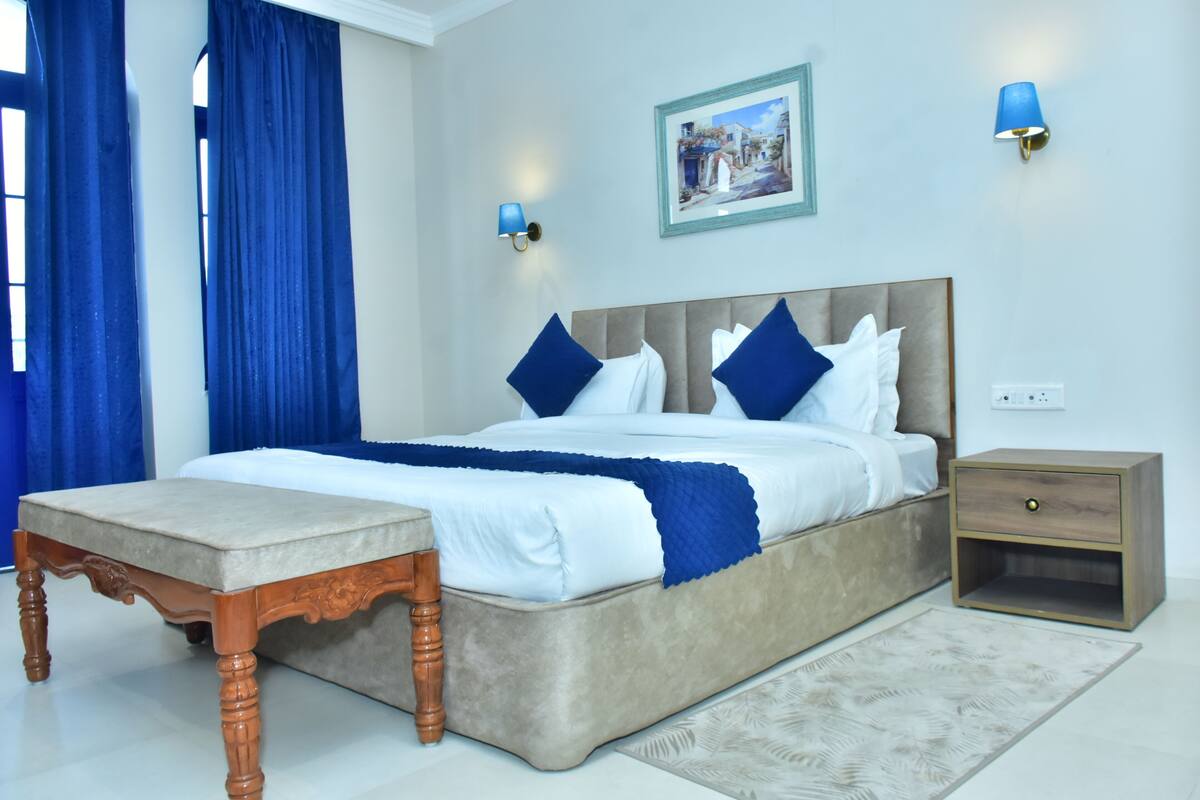 A bedroom with a bed, bedside table, nightstand, and a painting on the wall.