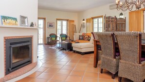 A spacious living room with a fireplace, wicker furniture, and a chandelier. - UA 78- Villa dos Sobreiros (Alcácer do Sal)