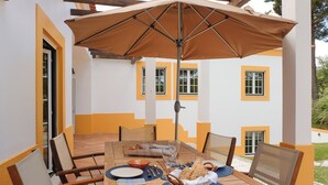 An outdoor dining area with a wooden table, chairs, and a large umbrella. - UA 78- Villa dos Sobreiros (Alcácer do Sal)