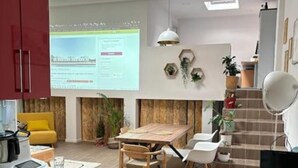 Una cocina moderna con comedor, un armario rojo, una mesa de madera y una pantalla de proyector mostrando una presentación.