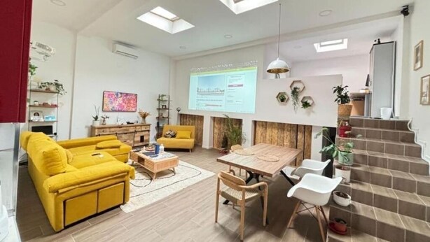 Una sala de estar moderna con un sofá amarillo, una mesa de comedor de madera y una escalera.