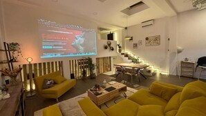 Una sala de estar moderna con una pantalla grande mostrando un video, una escalera y un comedor.