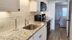 Una cocina con gabinetes blancos, encimera de granito, pileta de acero inoxidable y cocina a gas negra.