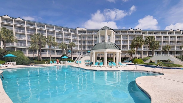 Un hotel con una piscina grande, un pabellón y un edificio de varios pisos con balcones.